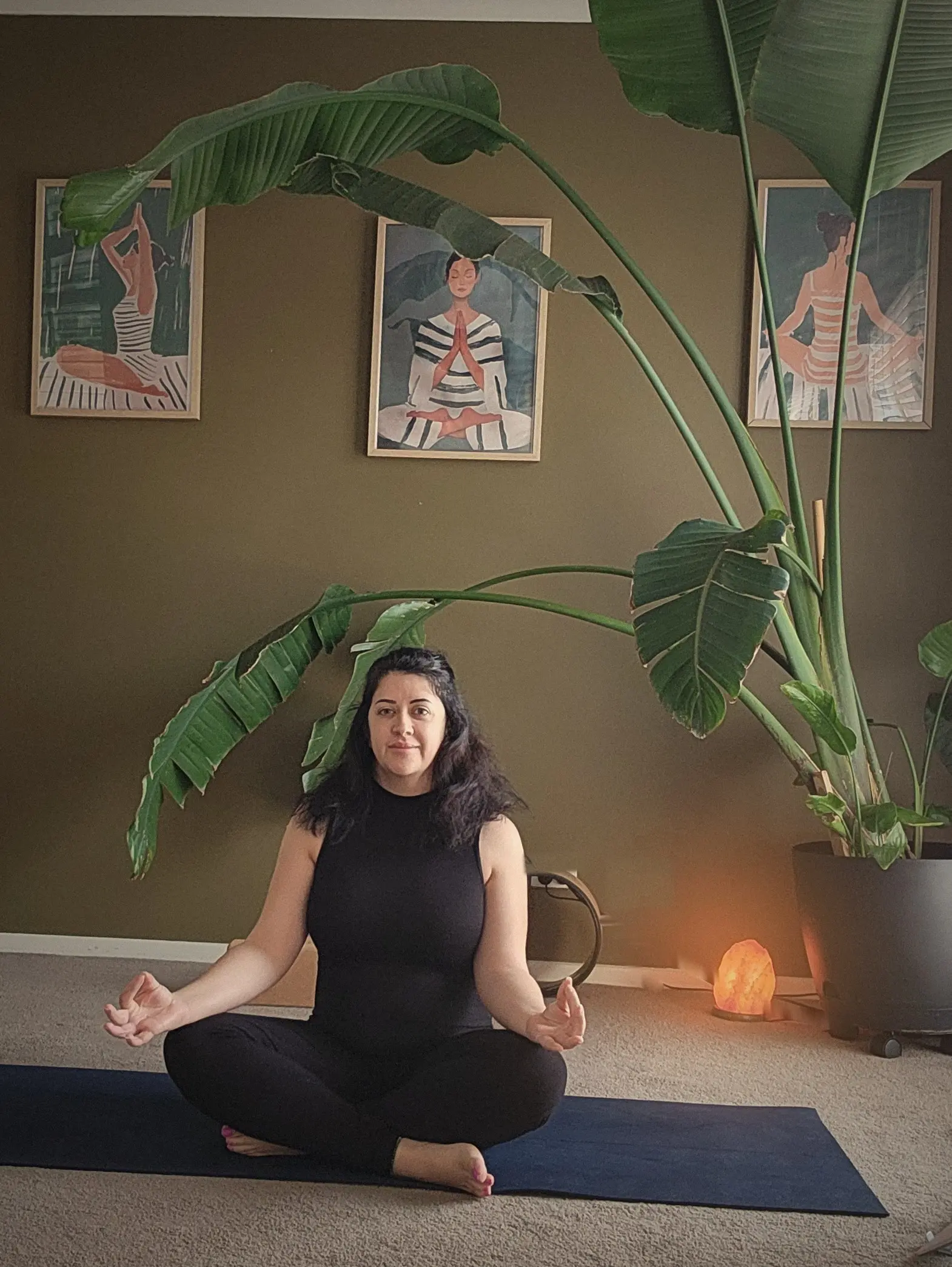 Carla seated in Sukhasana on her navy mat, hands resting on her knees, in her practice room.